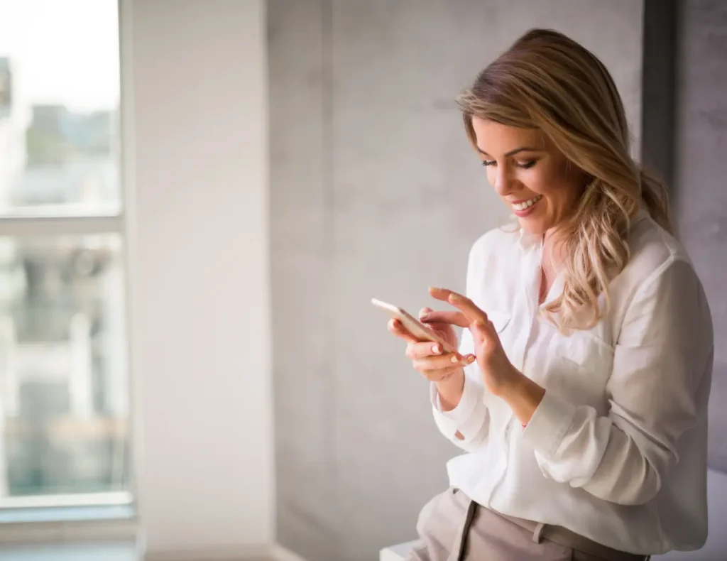 Smiling woman sitting while interacting with her smartphone for the Social Media service of the Digital Agency Jinni S.r.l.