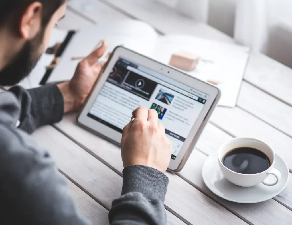 Man consulting a website on a tablet with a cup of coffee on the table for the service of Digital Agency Jinni S.r.l.