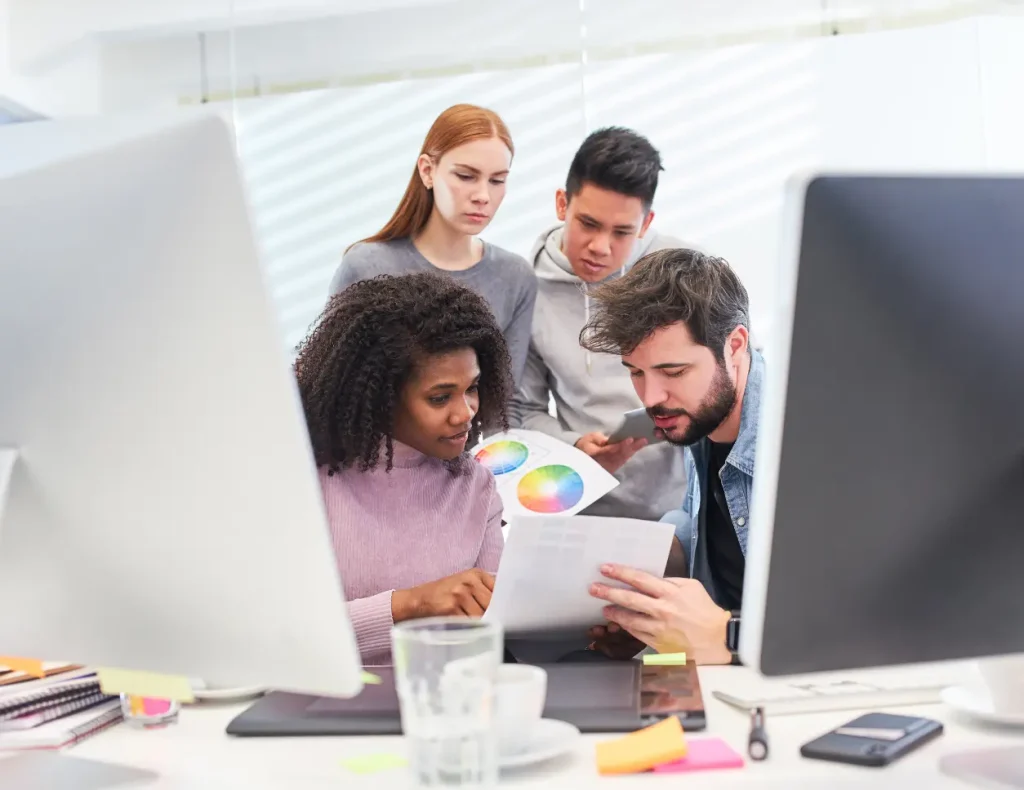 Multi-ethnic creative team works together on color palettes in front of computers.