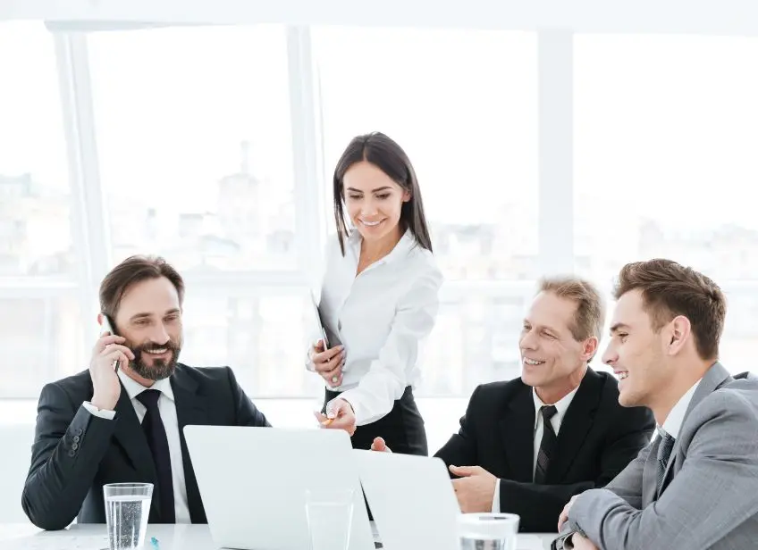 Meeting between four colleagues in formal attire, smiling around a laptop.