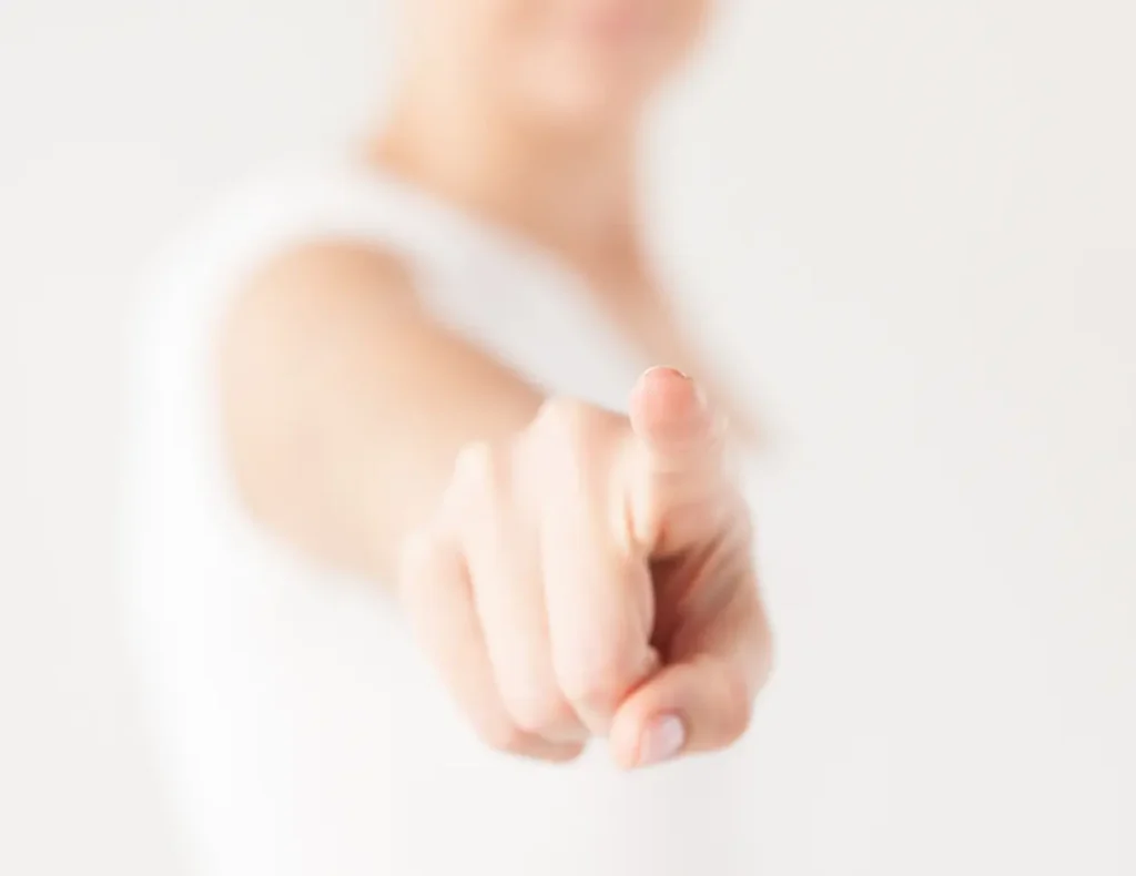 Hand pointed towards the lens, blurred and bright background.