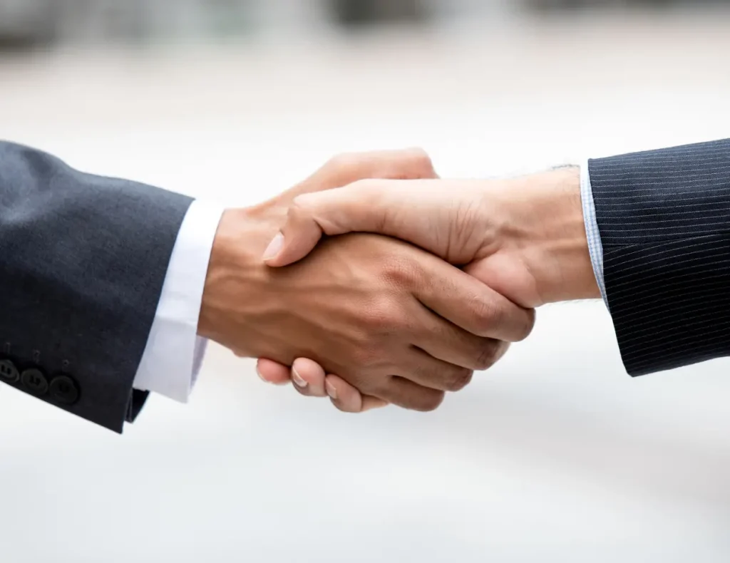 Two men in suits shake hands in a formal setting.
